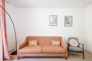 A room with a sofa and a chair, two framed artworks on the wall, and a floor lamp.
