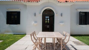 A white building with a tiled roof, a central doorway, and a table with chairs in front. - Casa São João a 400 Metros da Praia com Jardim (Arcozelo)