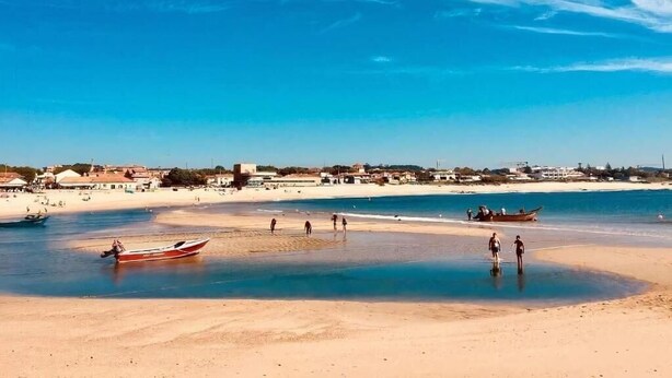 A beach with clear blue water, a boat, and people walking along the shore. - Casa São João a 400 Metros da Praia com Jardim (Arcozelo)