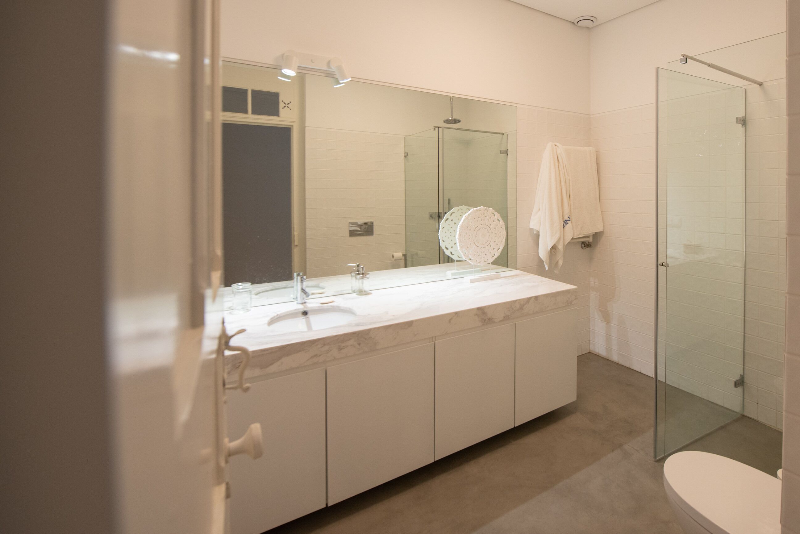 A modern bathroom with a large mirror, a sink, and a glass-enclosed shower.