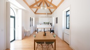 A spacious dining area with a wooden table and chairs, a kitchen in the background, and a high ceiling with exposed beams. - Casa São João a 400 Metros da Praia com Jardim (Arcozelo)