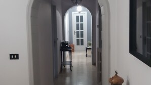 A hallway with an arched doorway leading to a room. There is a table with a lamp and a bottle on a shelf. - The Citrus Garden (San Marco Evangelista)