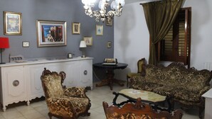 A room with a vintage sofa, a patterned armchair, a wooden coffee table, a white cabinet, and a chandelier. - The Citrus Garden (San Marco Evangelista)