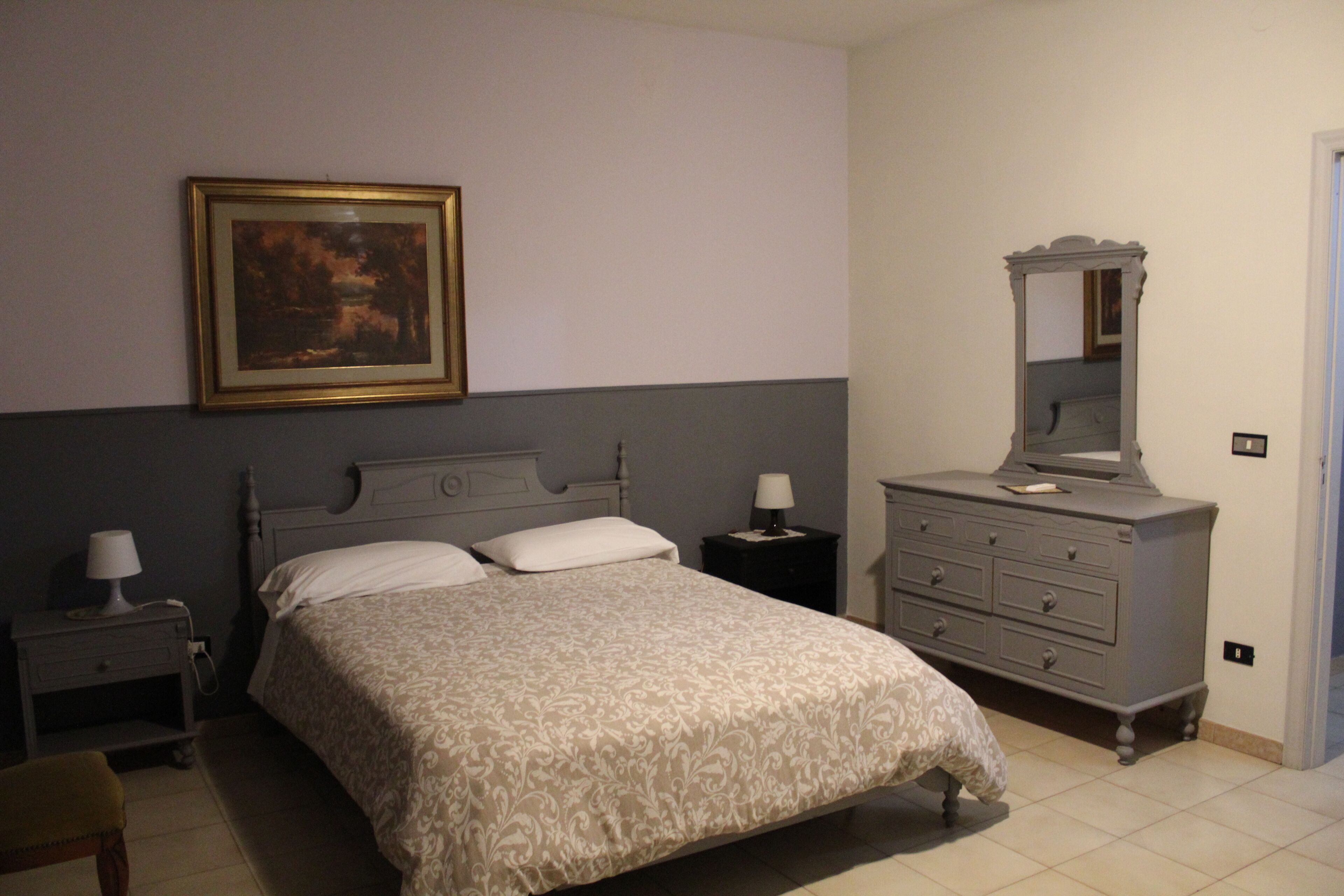 A bedroom with a bed, a dresser, a nightstand, a lamp, and a framed picture on the wall.