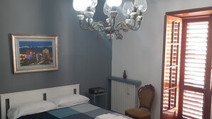 A bedroom with a bed, a chair, a radiator, a picture on the wall, and a chandelier. - The Citrus Garden (San Marco Evangelista)