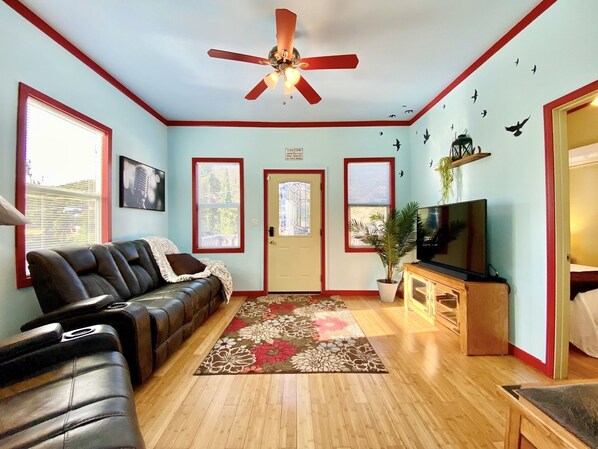 A living room with a sofa, TV, ceiling fan, and decorative wall stickers.