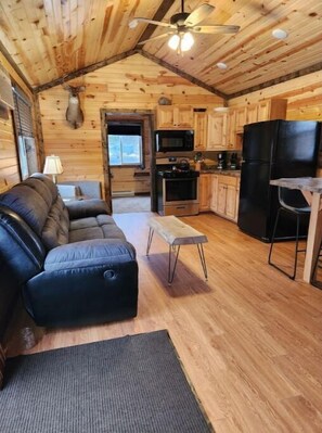 Cozy cabin interior with a black leather sofa, wooden bench, and modern kitchen appliances.