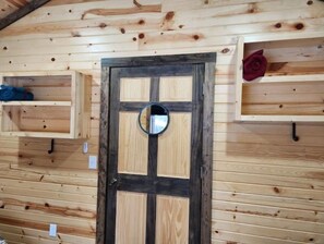 Features a central door with a circular mirror, a shelf with a decorative item, and a hook for hanging personal belongings.