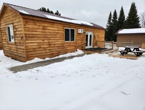 Cozy cabin with a front door, windows, and a porch area, perfect for outdoor dining and relaxation.
