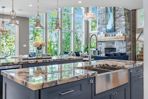 A modern kitchen with a large island, stone fireplace, and large windows.