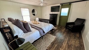 Une chambre à coucher comprenant un lit, une chaise, une commode, un téléviseur et un ventilateur de plafond.