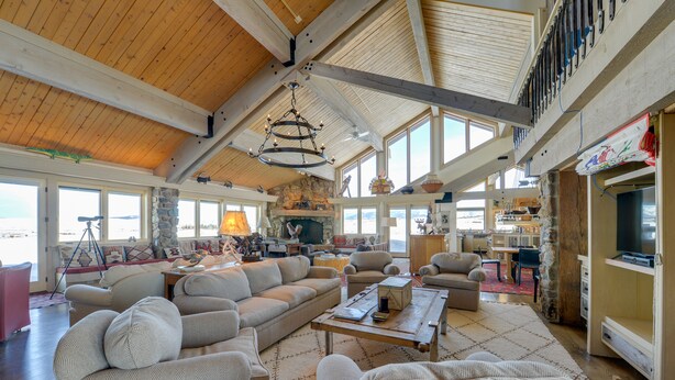 A spacious living area with a high ceiling, large windows, and a stone fireplace. - Cora Home w/ Mountain Views - Fishing On-Site! (Cora)