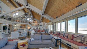 A spacious living area with a high ceiling, wooden beams, a large window overlooking a snowy landscape, and a cozy seating arrangement. - Cora Home w/ Mountain Views - Fishing On-Site! (Cora)