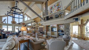 A spacious living area with a high ceiling, a chandelier, and a balcony with a railing. - Cora Home w/ Mountain Views - Fishing On-Site! (Cora)
