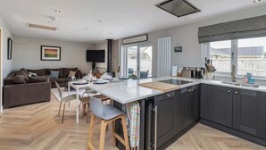 A modern kitchen with a central island, dark cabinetry, and a large window. - Family-Friendly Retreat between Beach & Mountains (Morfa Bychan)