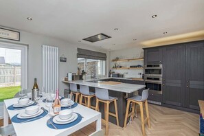 Una cocina moderna con una isla central, taburetes de bar y un comedor preparado para seis personas.