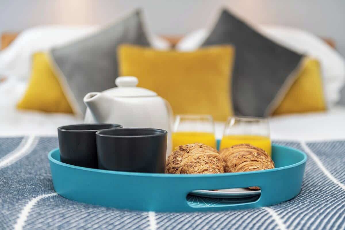 A breakfast tray with a teapot, two cups, a glass of orange juice, and two croissants on a blue tray.