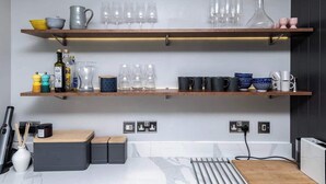 A kitchen with two wooden shelves holding various glassware and kitchen items. There are also two electrical outlets and a kettle on the countertop. - Family-Friendly Retreat between Beach & Mountains (Morfa Bychan)