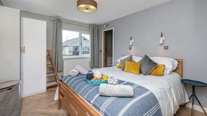 A bedroom with a bed, bedside table, lamp, and a window. - Family-Friendly Retreat between Beach & Mountains (Morfa Bychan)