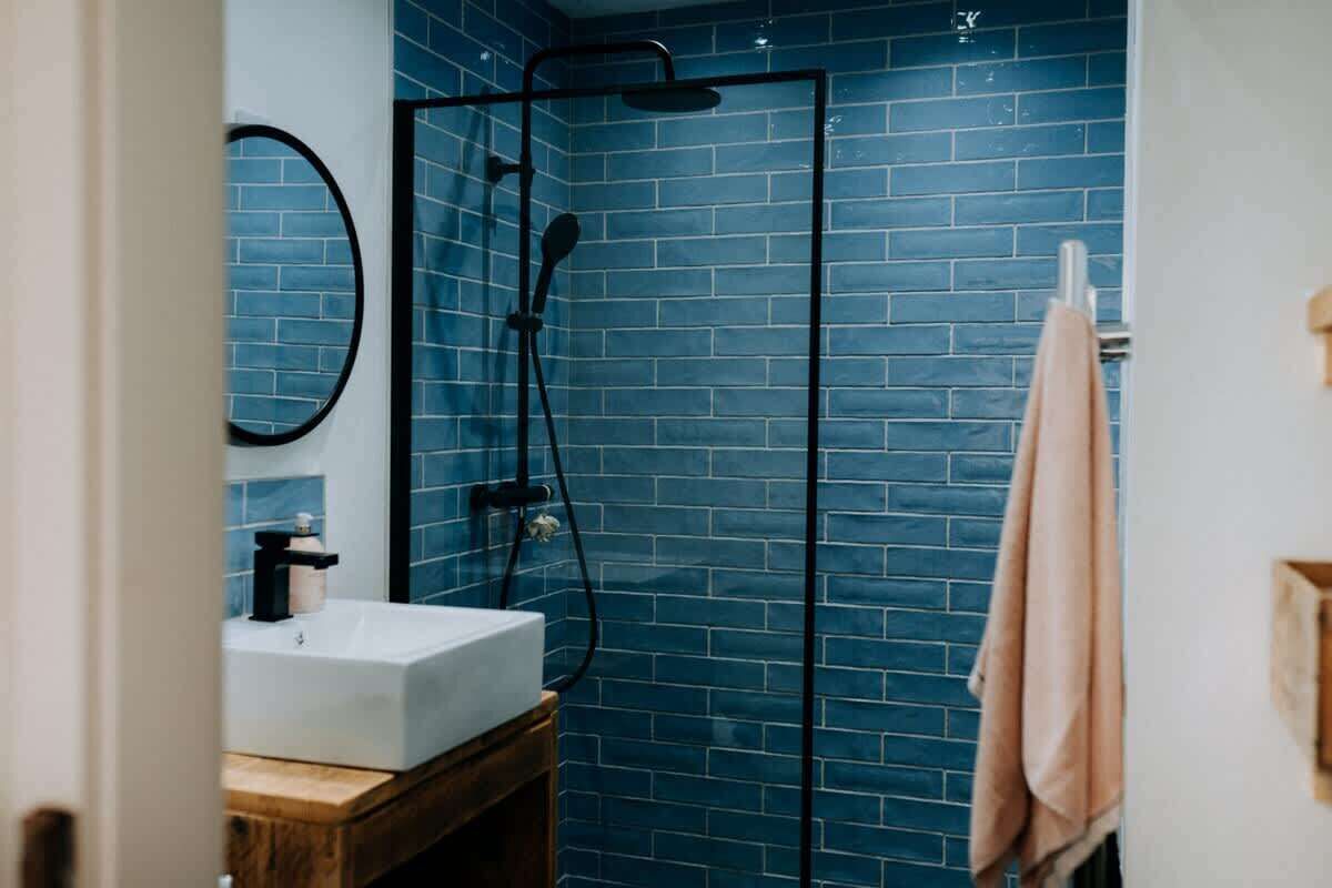 A bathroom with a blue-tiled shower enclosure, a white sink, and a wooden vanity.