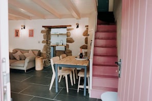 A cozy living area with a stone wall, a wooden dining table, and a pink staircase.
