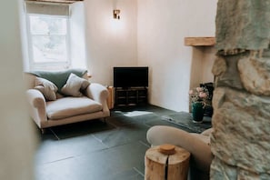 A cozy living room with a beige sofa, a television, and a stone wall.