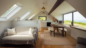 Une chambre confortable aménagée en mezzanine, avec un grand lit, une table à manger et une vue sur l’extérieur.