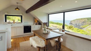 Une cuisine moderne avec une table en bois, des armoires blanches et une grande fenêtre donnant sur un paysage côtier.
