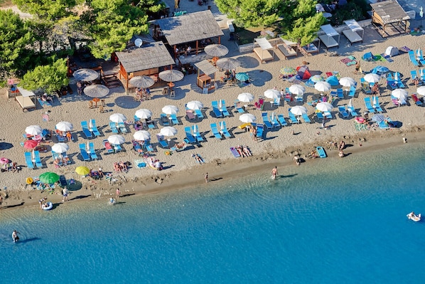 Vista aérea de una playa con numerosos sombrillas, sillas de playa y una pequeña estructura de madera.