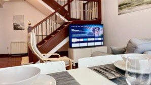 Ein modernes Wohnzimmer mit einer Holztreppe, einem Flachbildfernseher, einem Esstisch mit Schüssel, Besteck und einem Glas Wasser.