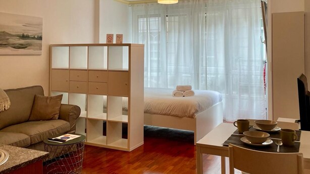 Ein gemütlicher Raum mit Holzboden, einem Bett mit weißer Bettwäsche, einer Couch, einem kleinen Tisch mit Stuhl und zwei Pendelleuchten.