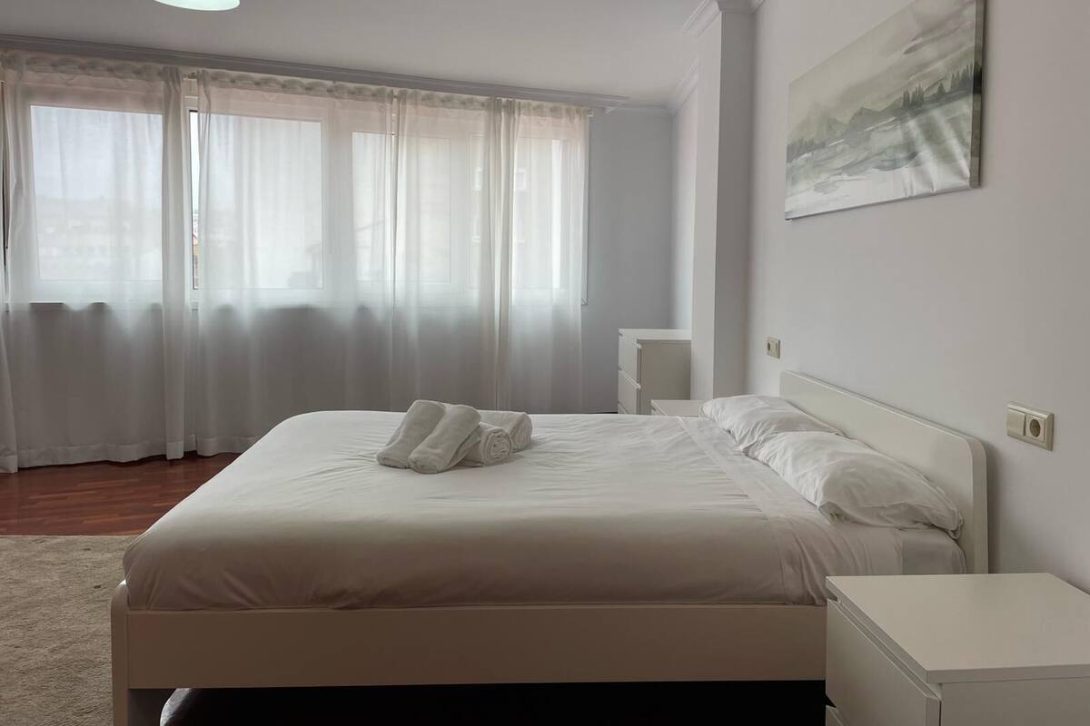 Una cama bien hecha con sábanas y toallas blancas, una mesita de noche y un cuadro en la pared.
