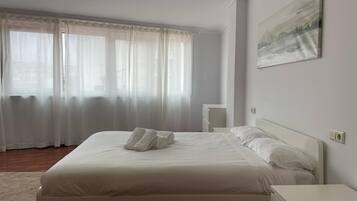 A neatly made bed with white linens and towels, a bedside table, a nightstand, and a painting on the wall.