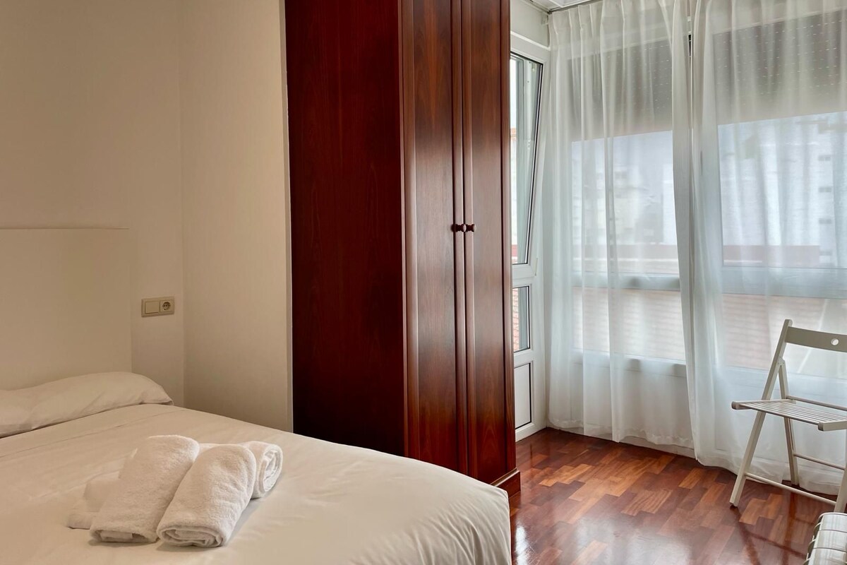 Een hotelkamer met een bed, een kledingkast, een stoel en een raam met dunne gordijnen.