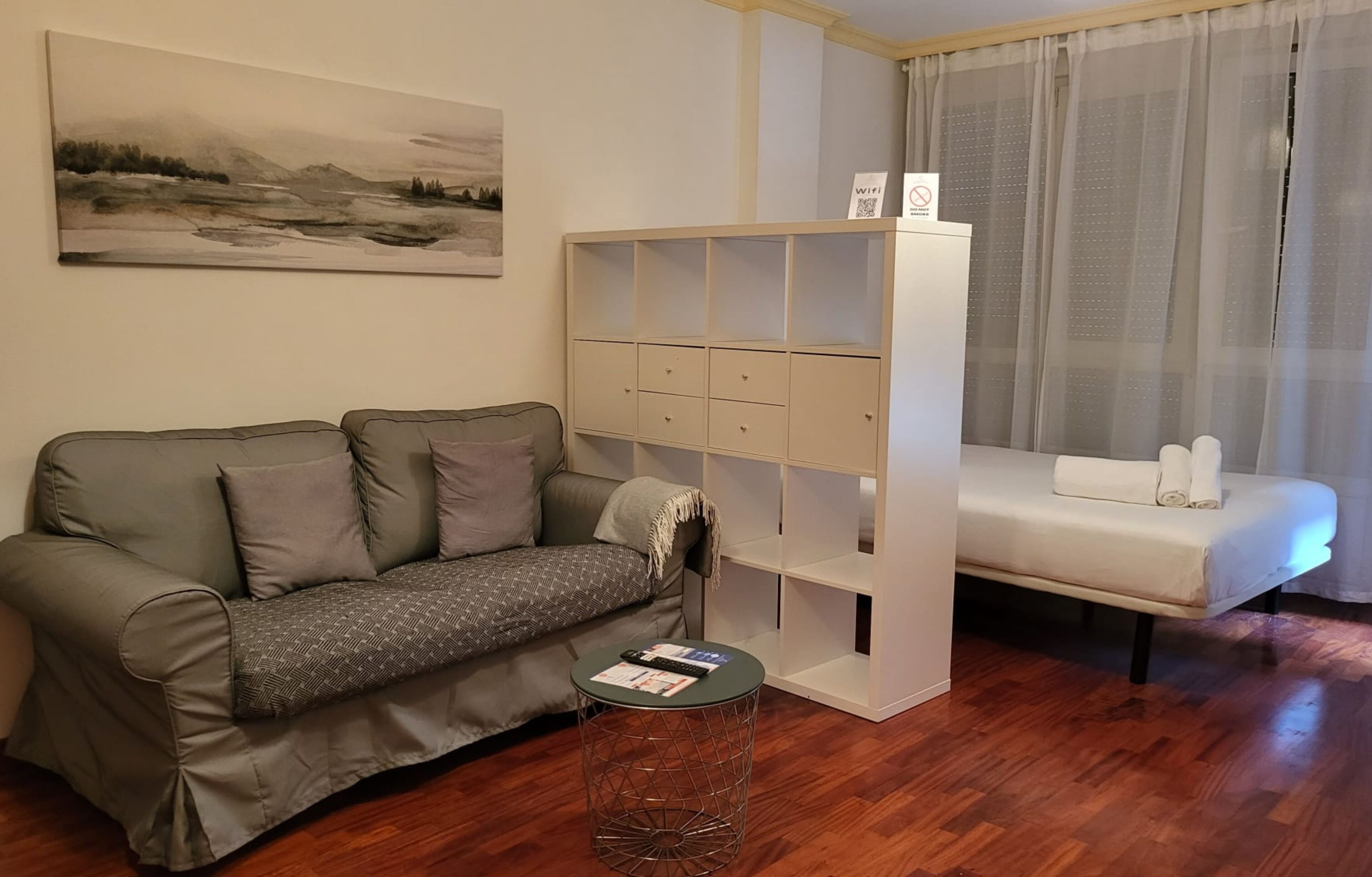 Un soggiorno moderno con un divano, un tavolino, una libreria bianca e un letto.