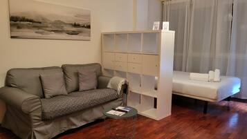 Un soggiorno moderno con un divano, un tavolino, una libreria bianca e un letto.