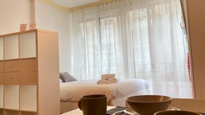 Ein Hotelzimmer mit einem Bett, einem Nachttisch mit Schalen und einem Löffel, einem Kleiderschrank und einem Fenster mit transparenten Vorhängen.