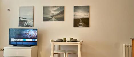 A living room with a TV, a dining table, and three wall-mounted paintings.
