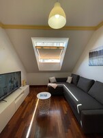 A modern living room with a sloped ceiling, a television, a sofa, a coffee table, and a skylight.