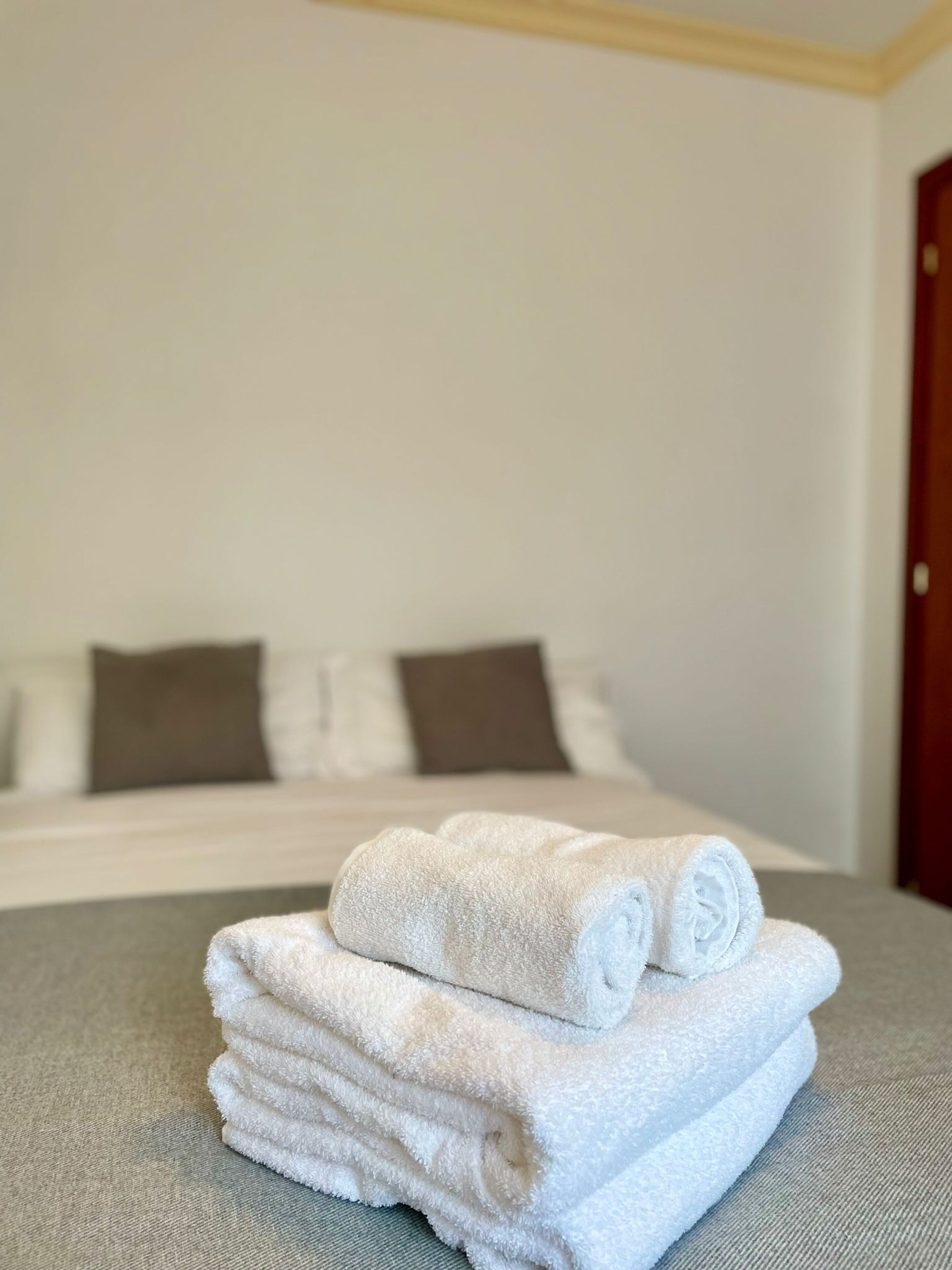 A neatly made bed with white and brown pillows, a stack of white towels, and a wooden door in a hotel room.