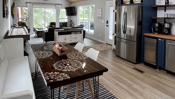 Una cocina amplia con vigas de madera, un candelabro, un comedor con una mesa estampada y un refrigerador.