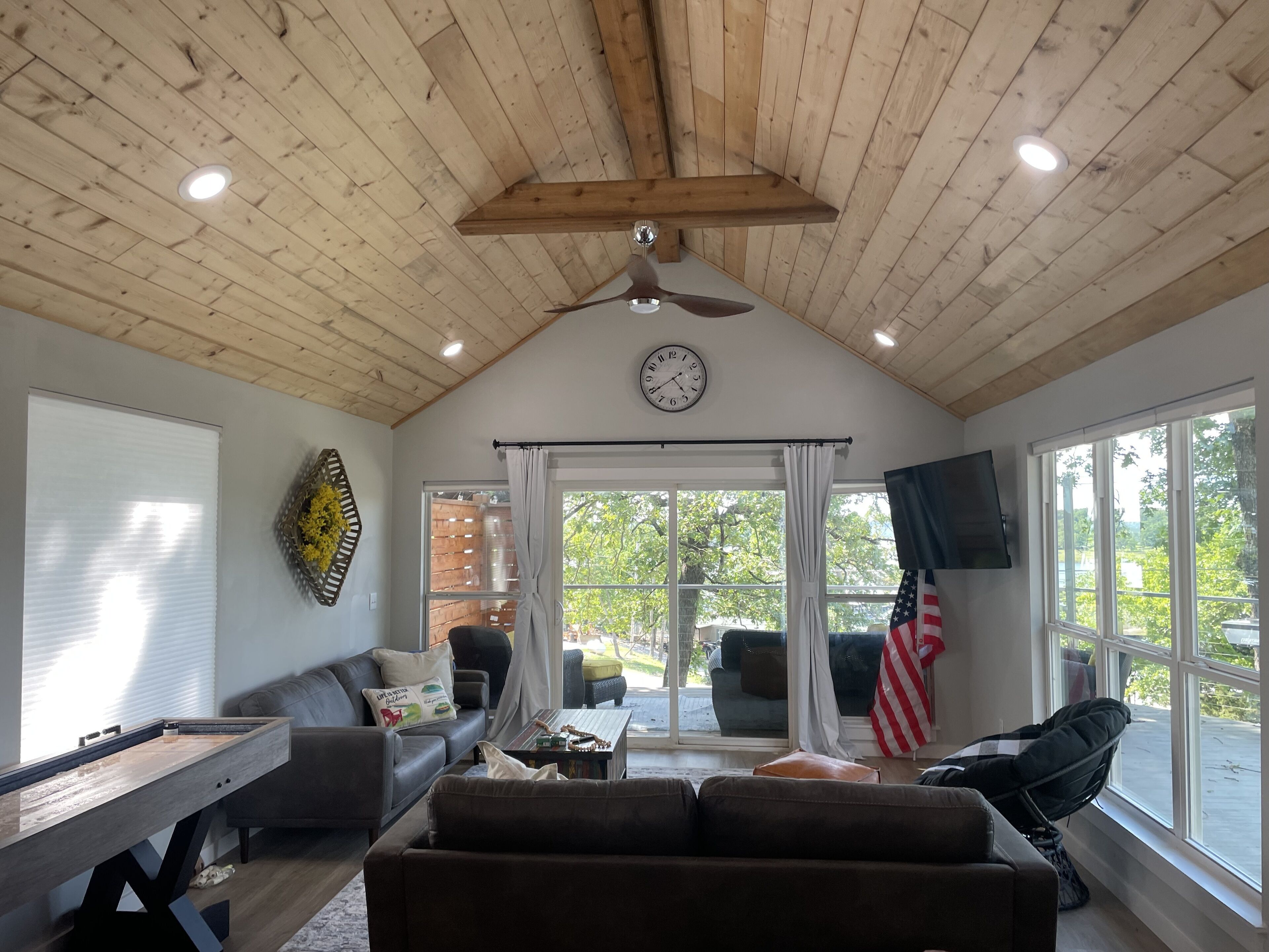Una sala de estar acogedora con techo de madera, un ventanal grande, un televisor de pantalla plana y una mesa de comedor.