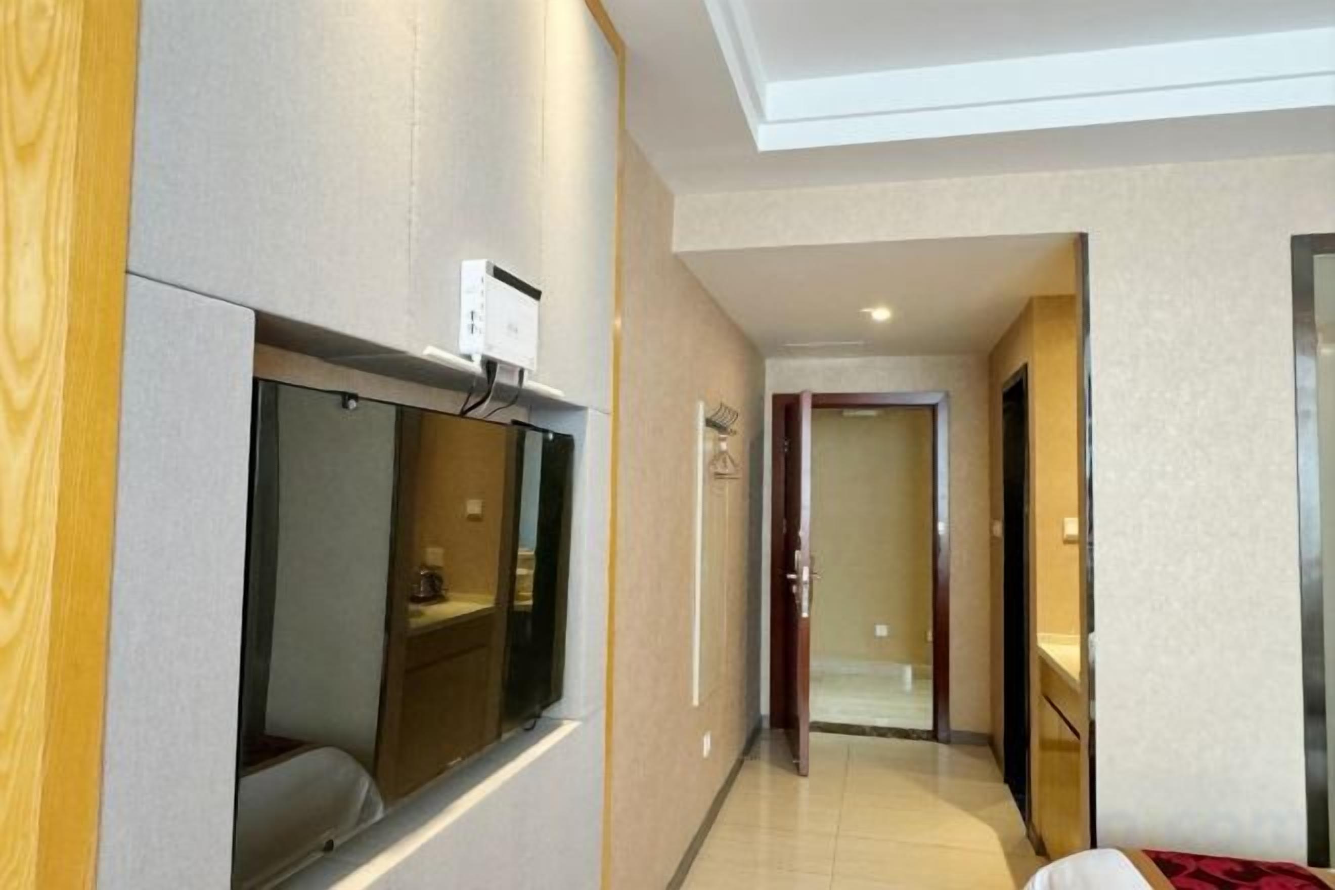 Pasillo de hotel con un muro espejado, una zona de recepción y una puerta que da a otra habitación.