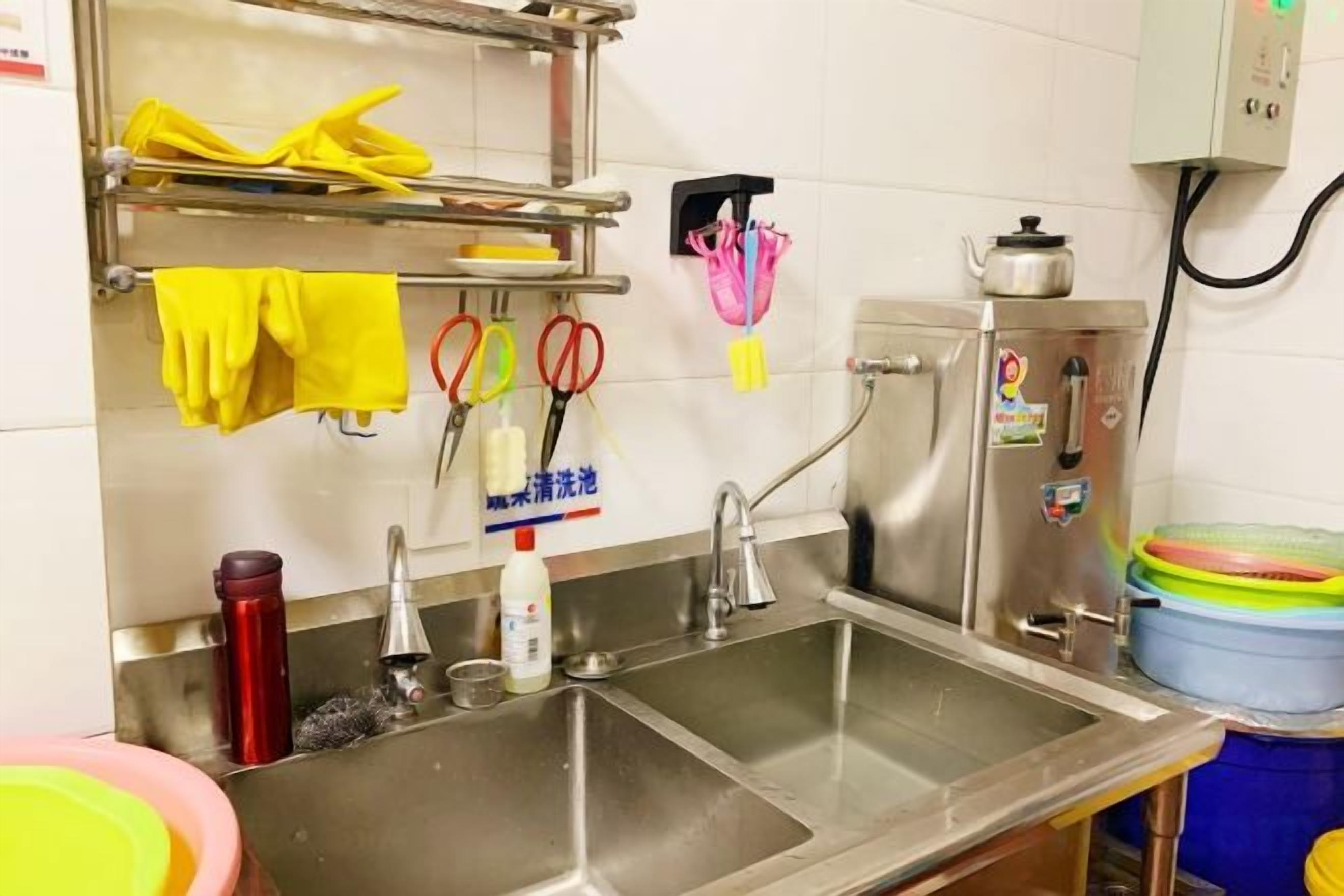 A kitchen with stainless steel sinks, a dish rack, and various kitchen utensils.