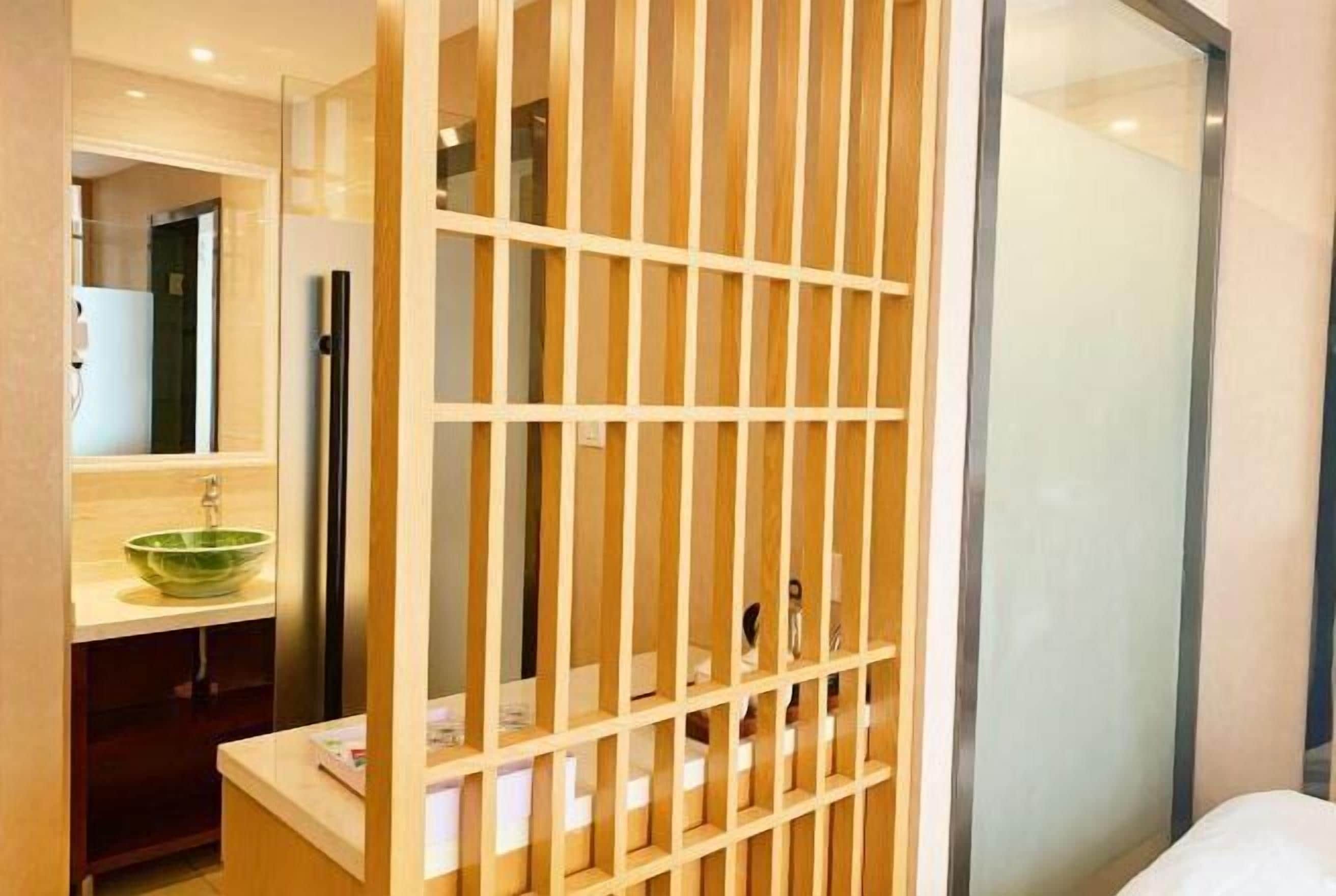 A hotel room with a wooden partition, a sink with a green bowl, and a bed with white bedding.