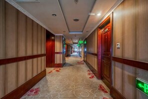 Un couloir dâhĂŽtel avec un tapis Ă motifs, des lambris en bois et un panneau de signalisation de sortie vert.