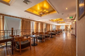 Um restaurante espaçoso com piso de madeira, várias mesas e cadeiras, e um candelabro.