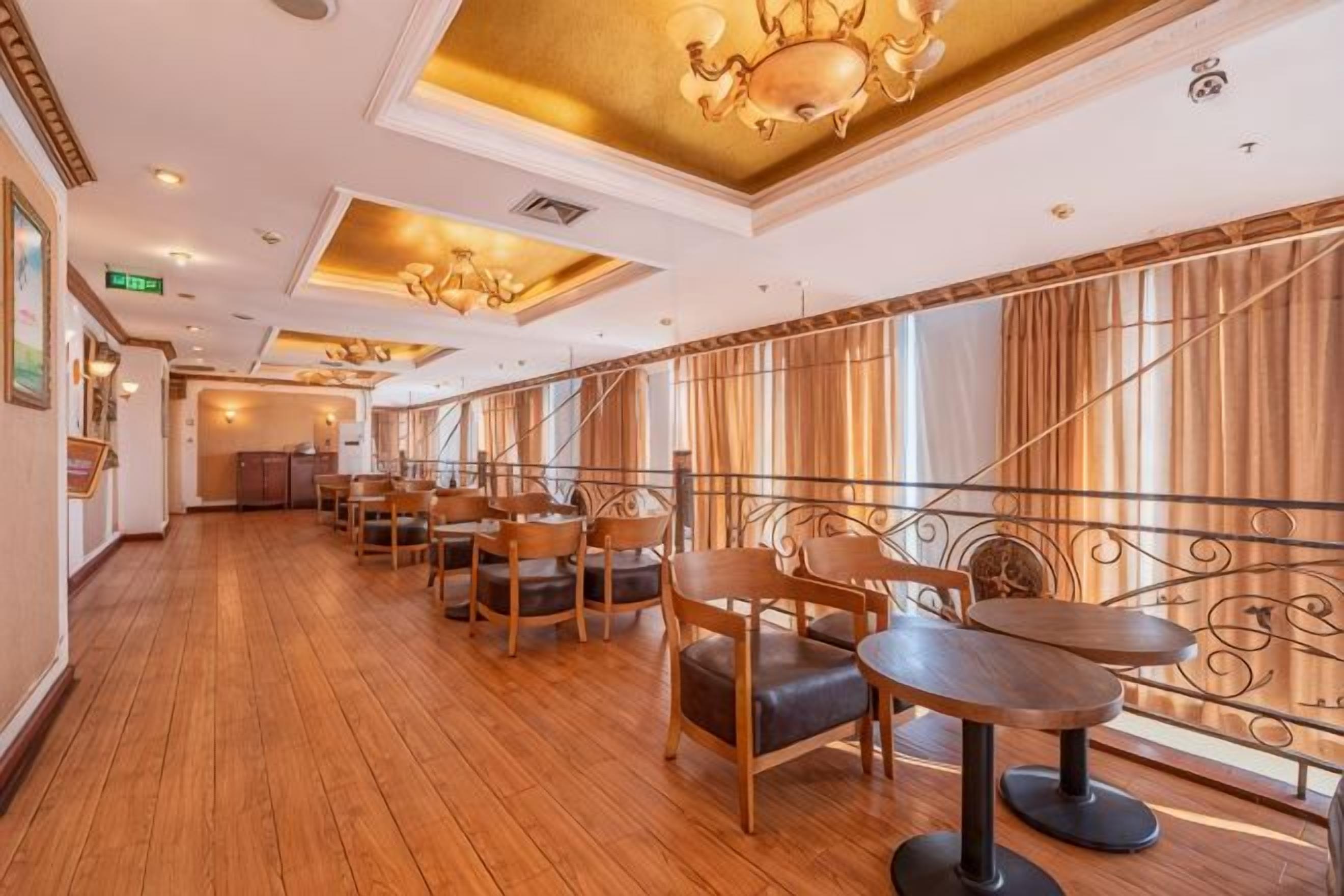 A dining area with wooden tables and chairs, a chandelier, and large windows with curtains.
