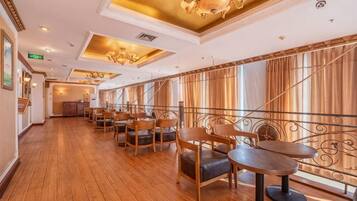 A dining area with wooden tables and chairs, a chandelier, and large windows with curtains.