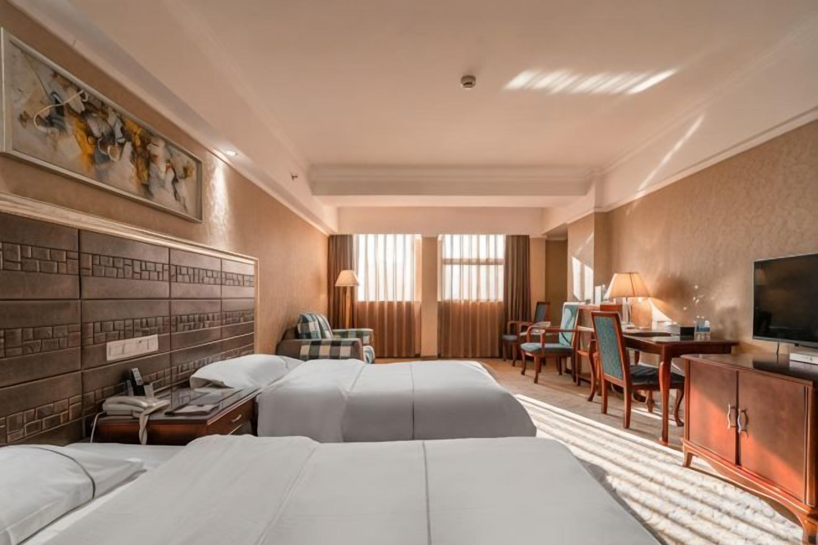 A hotel room with two beds, a desk, a chair, a TV, and a painting on the wall.